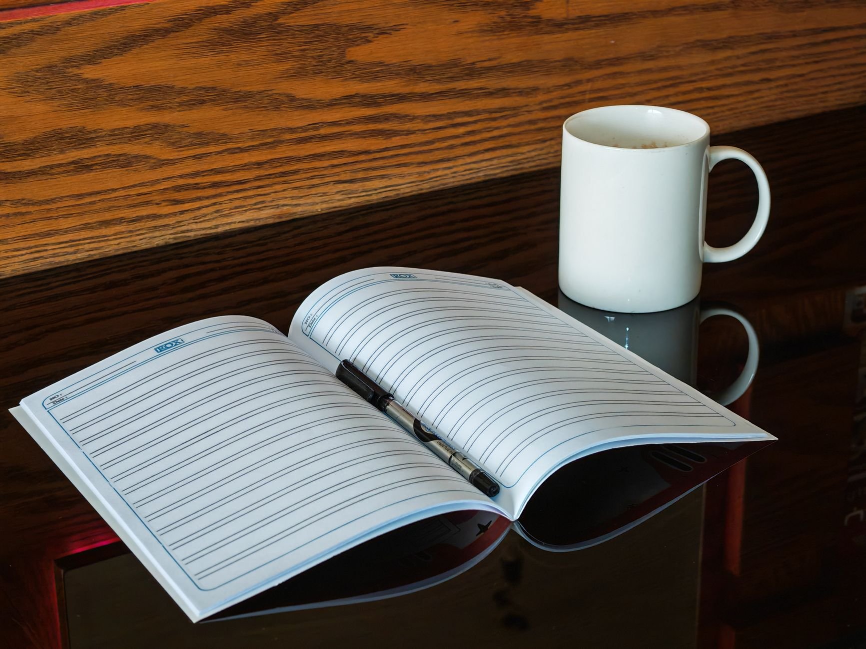 An open notebook with a pen beside a coffee mug — the quiet ritual of reading and reflection.